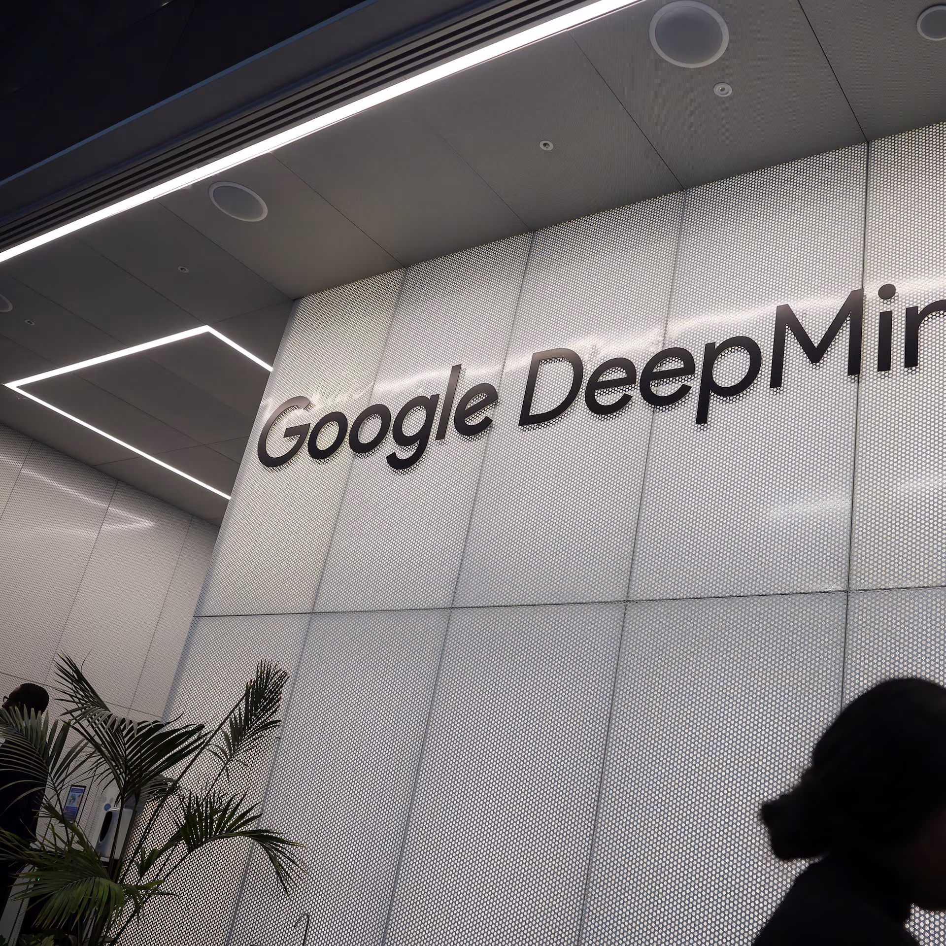 A partial view of a wall with the Google DeepMind logo and some plants at the bottom left corner.